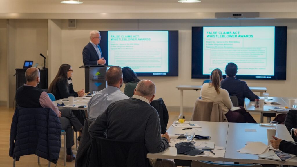 Attendees at the Rutland Regional Medical Center (RRMC) event gather in The Hub CoWorks’ large, tech-enabled Streetside Conference Room in downtown Rutland, Vermont. The modern coworking space features collaborative seating, state-of-the-art Cisco Webex technology for hybrid meetings, and three large screens displaying healthcare data and presentations, including topics like the False Claims Act. The room’s sleek design, natural light, and professional yet welcoming atmosphere make it ideal for events, meetings, and presentations.